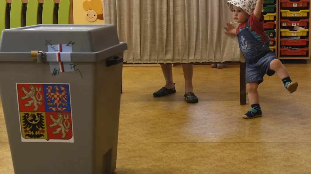 Dítě čeká, až jeho matka za plentou vloží svůj hlas do obálky