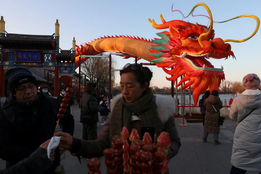 Žena si kupuje dezert tanghulu od prodavače před instalací draka v čínském Pekingu