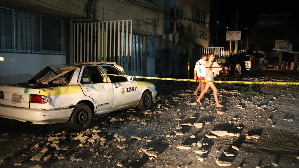 Pár míjí taxík, který byl poškozen padajícími úlomky po silném zemětřesení v mexickém Acapulcu