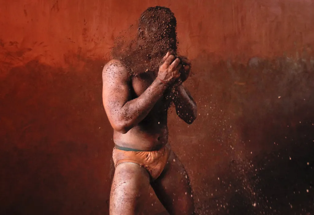 Wrestler si potírá ruce bahnem, aby se mu během tradičního „bahenního“ zápasu Kushti nepotily a neklouzaly. Během posledních let tradiční sport mladí lidé opouští a obrací se spíše k té verzi, v níž mohou soutěžit v mezinárodní konkurenci. Mumbai, Indie, 2012