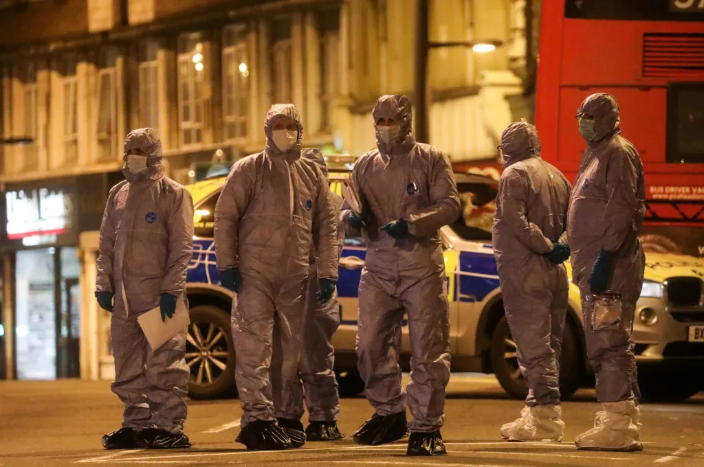 Muži v ochranných oblecích nejsou členové zdravotnických týmů v oblastech zasažených koronavirem, ale policejní forenzní tým. Ten řešil případ muže, který byl zastřelen policisty poté, co zaútočil nožem na dva kolemjdoucí na Streatham High Road v jižním Londýně