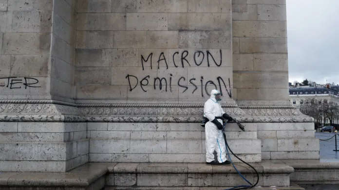 Muž se chystá odstranit nápis na Vítězném oblouku, který požaduje demisi prezidenta Macrona.