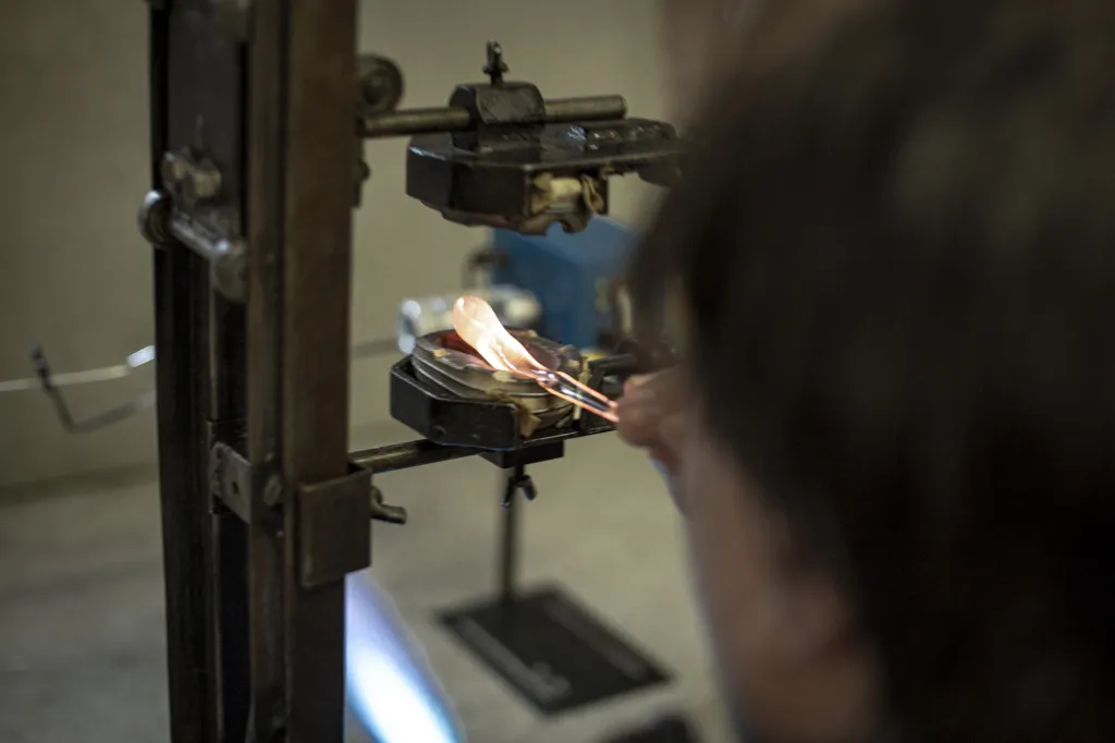 Tou první je příprava keramických forem. Ty se připevní na stojan a plastické sklo se nafoukne do formy