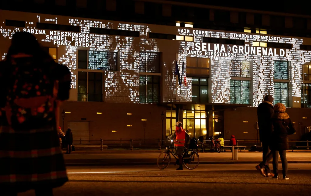 Lidé sledují světelnou instalaci, která na fasádě francouzského velvyslanectví v Berlíně ukazuje jména obětí nacistického režimu