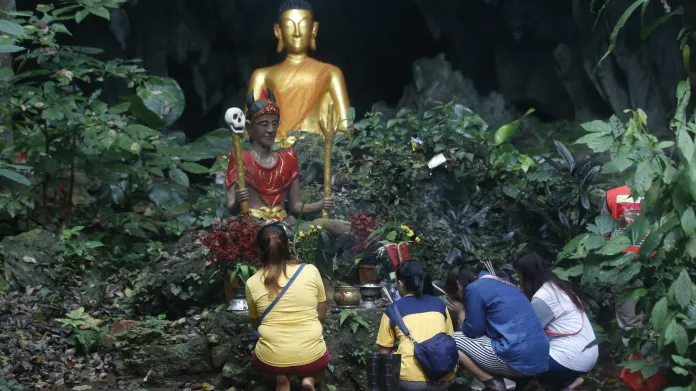 Členové rodiny se modlí před buddhistickou sochou v blízkosti jeskyně