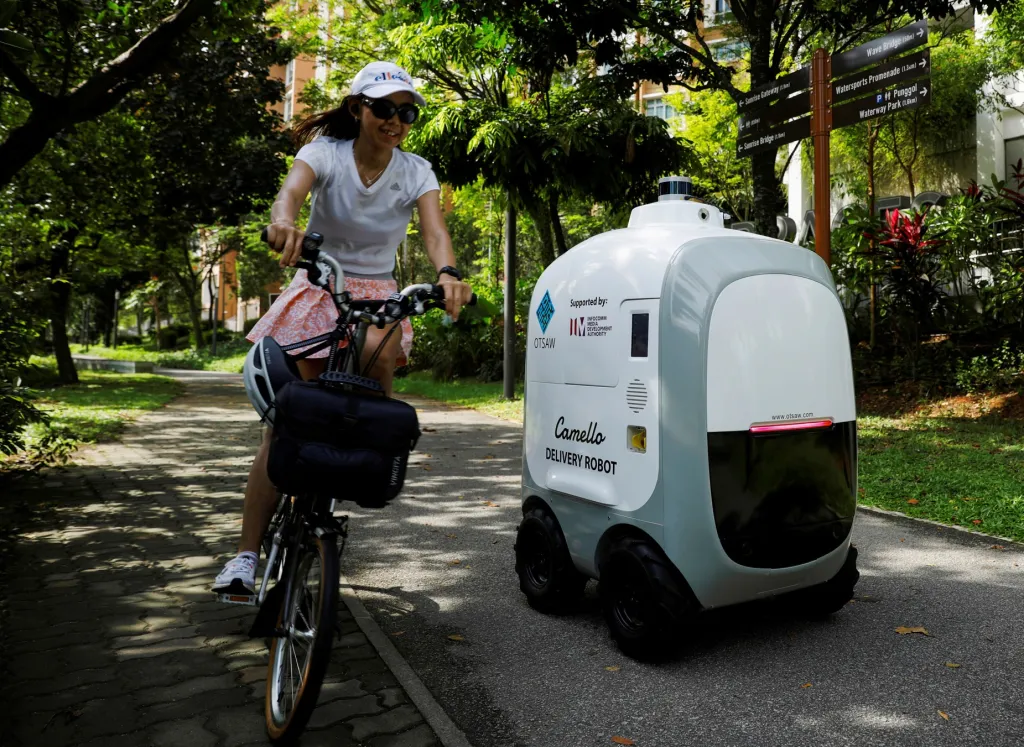 Autonomní roboti si razí cestu Singapurem. Projíždějící cyklista míjí robota, který je určen k rozvážce potravin