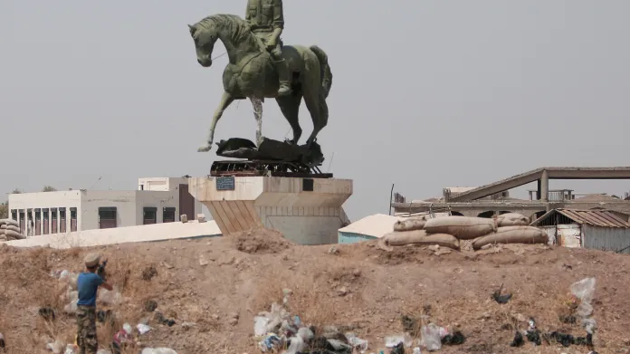 Kurdský bojovník střílí na sochu bratra syrského prezidenta Asada ve městě Hasaká