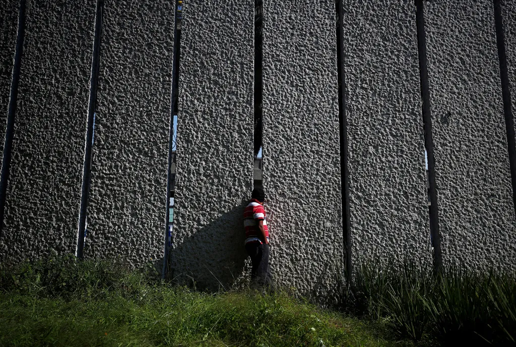 Uprchlík, jeden z tzv. karavany migrantů směřující z Latinské Ameriky do USA, se dívá dírou ve zdi v uprchlickém táboře do ulic města Mexico City.