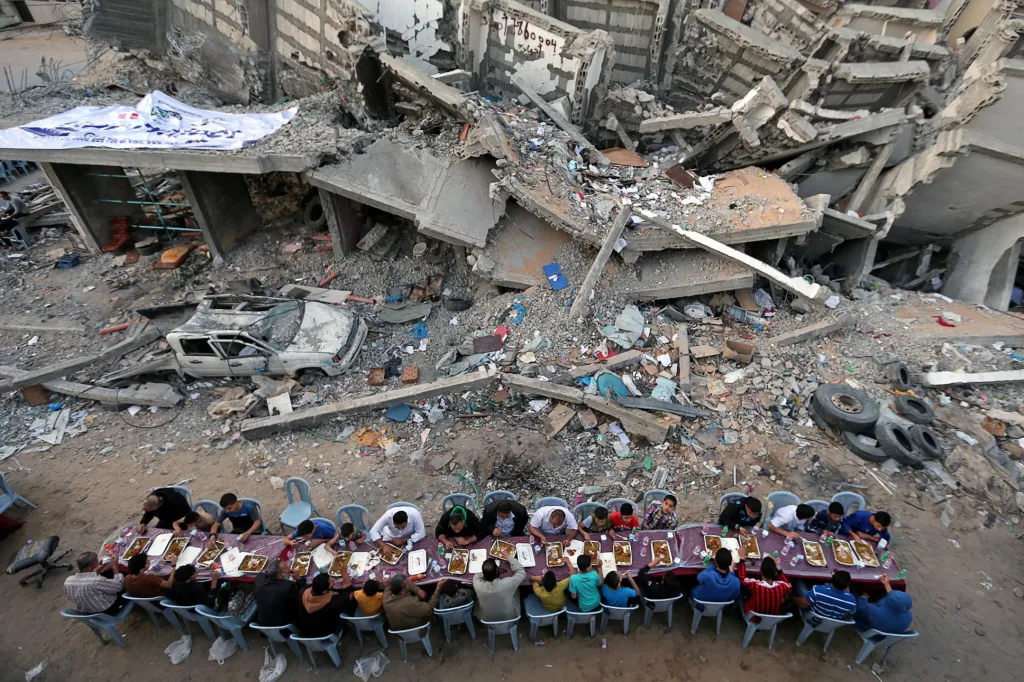 Palestinci usedají ke společnému stolu po skončení svatého měsíce ramadánu poblíž sutin budovy nedávno zničené izraelským leteckým úderem v Pásmu Gazy