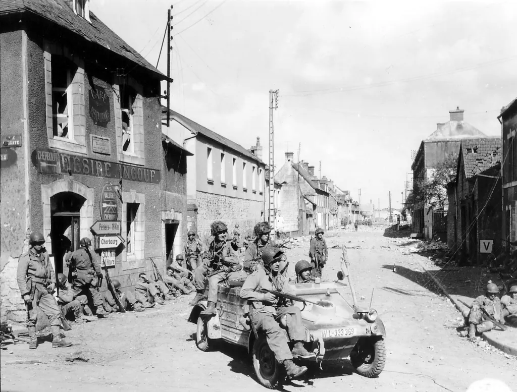 Vojáci 101. výsadkové divize řídí zajatý německý vůz Kubelwagen na křižovatce Rue Holgate a RN13 v Carentanu 6. června 1944