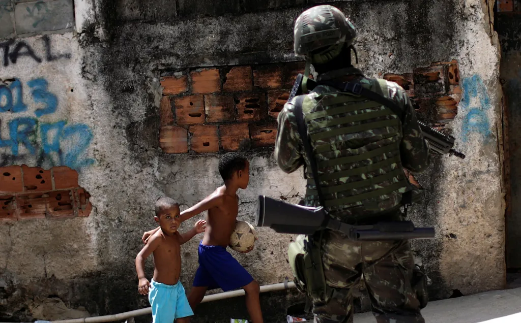 Děti pozorují brazilského ozbrojeného vojáka, který se účastní operace proti drogovým gangům ve slumu Lins v Riu de Janeiru.