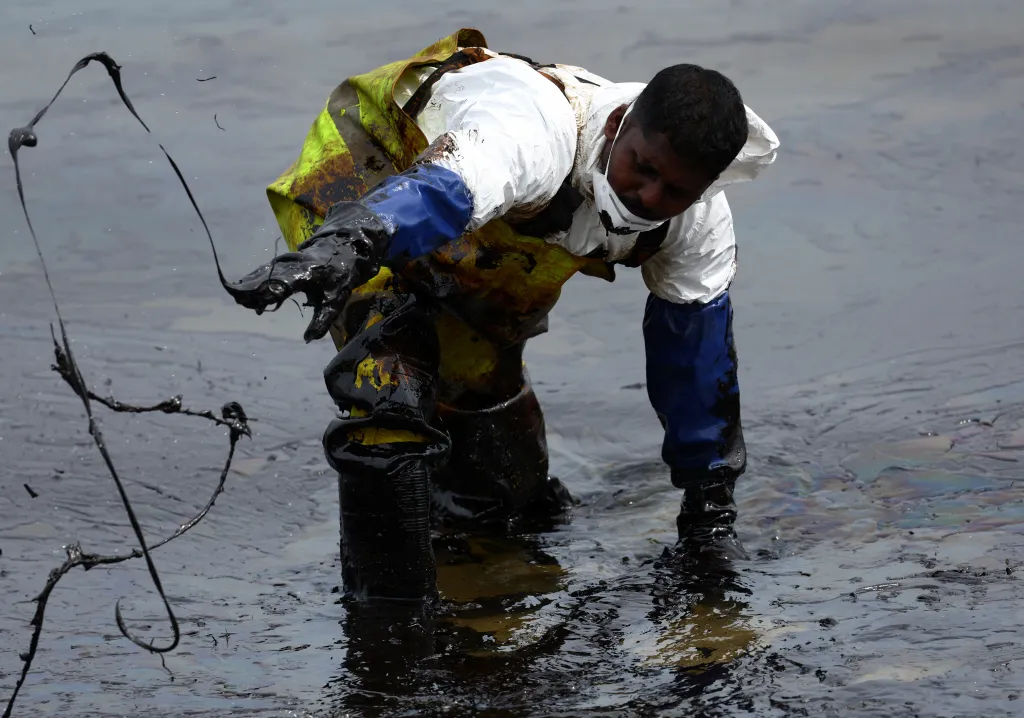 Pracovník obsluhuje čerpadlo při odstraňování ropné skvrny na pláži Tanjong