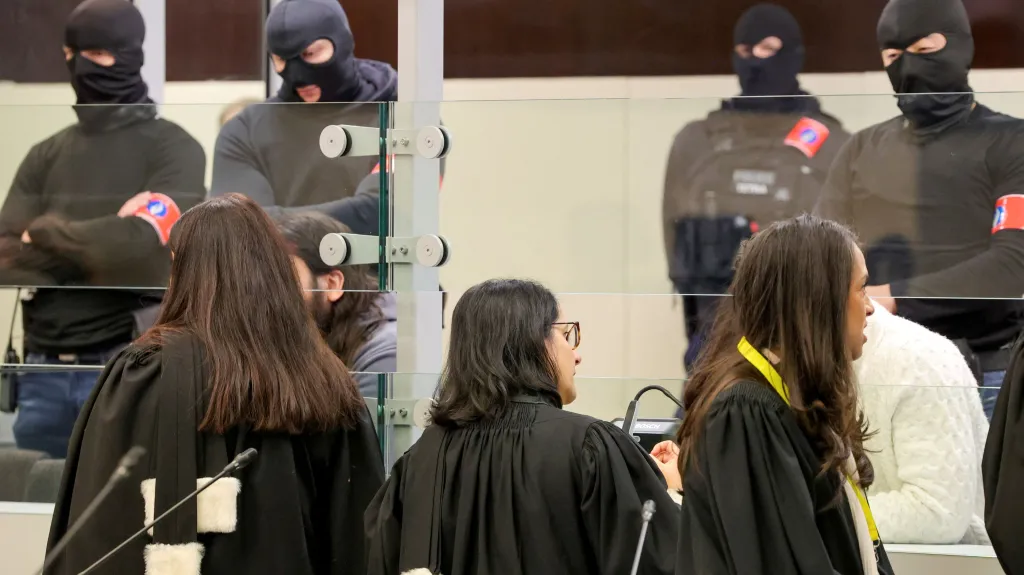 Obhájci mluví s obžalovanými, kteří jsou v části soudní síně oddělené sklem