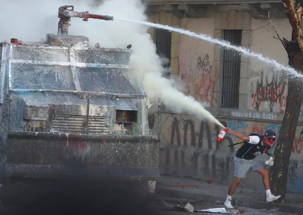 Jeden z protivládních demonstrantů stříká hasicím přístrojem na policejní transportér během nepokojů v chilském hlavním městě Santiagu