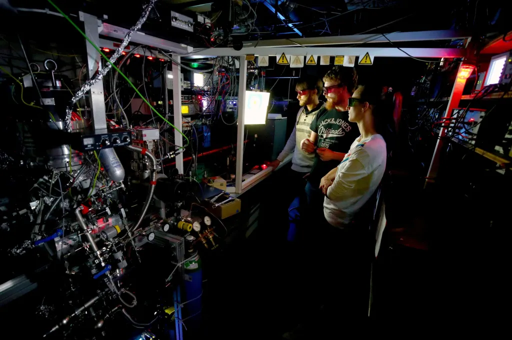 Studenti fyziky Julian Robertz, Maximilian Schmidt a Lisa Ringenová diskutují o výsledcích systému Atom Trap Trace Analysis (výzkum stability izotopů, který zjišťuje stáří ledu) v laboratoři ArTTA v Kirchhoffově ústavu pro fyziku v Heidelbergu v Německu