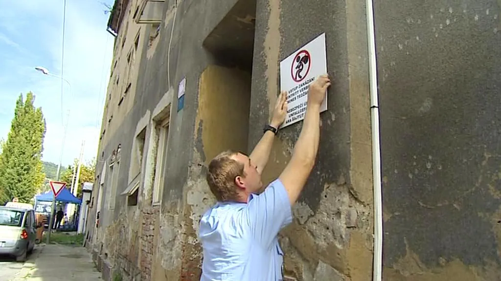 Strážník vyvěšuje na dům ceduli Zákaz vstupu