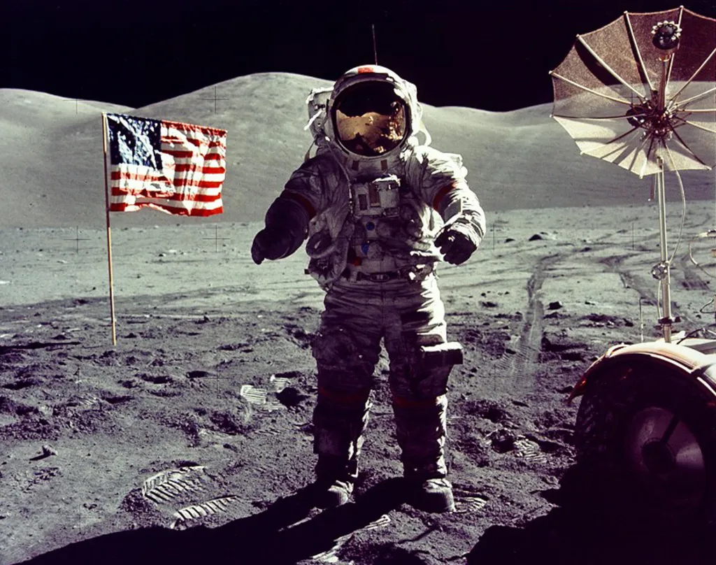 Astronaut Eugene Cernan kráčí k lunárnímu vozítku poblíž americké vlajky