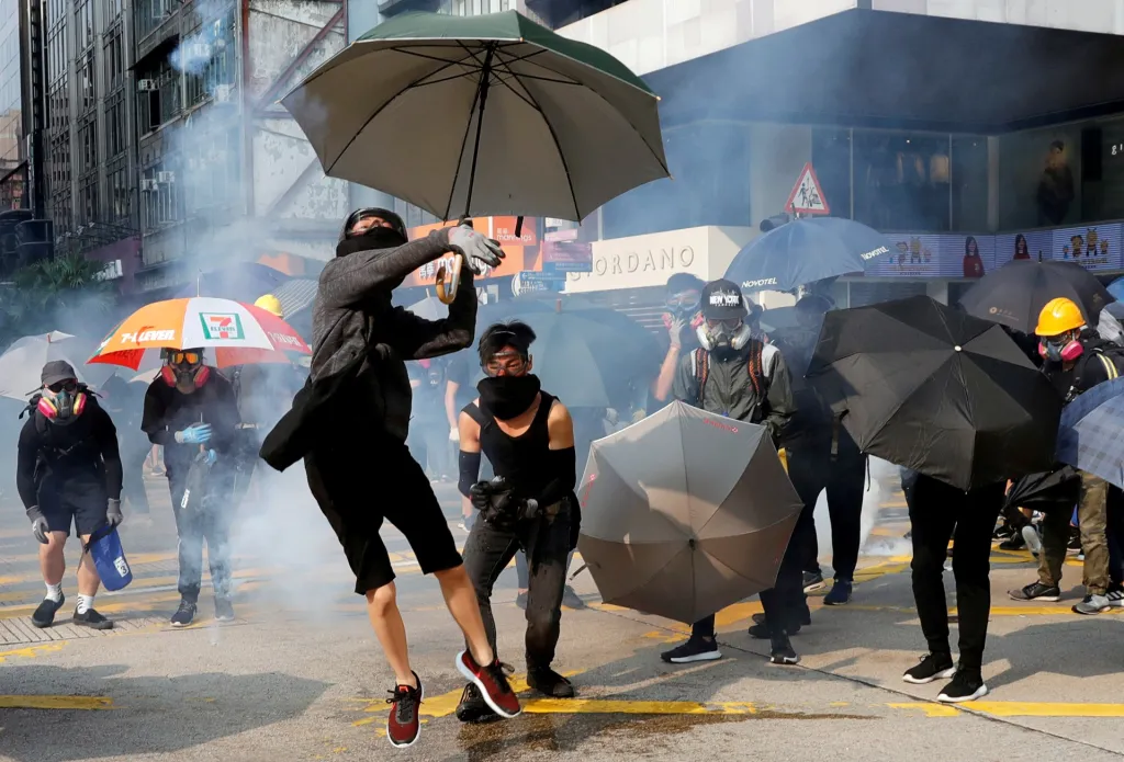 Situace v ulicích Hongkongu se rovněž nezklidňuje. Na snímku řada protivládních demonstrantů bojuje s deštníky proti dopadajícím plynovým granátům