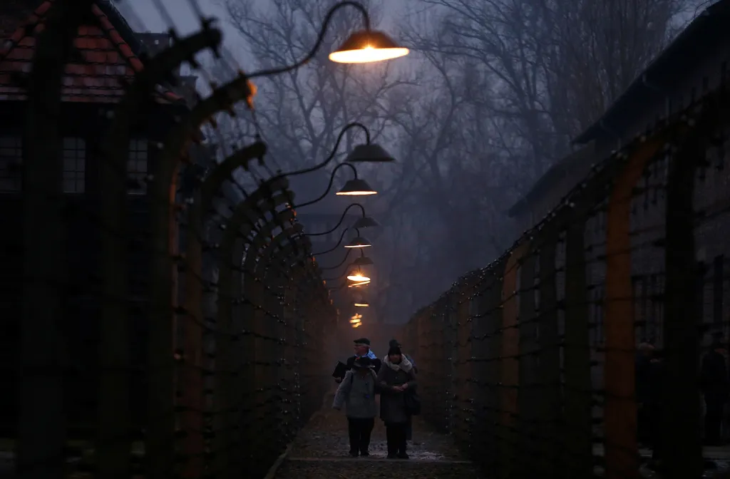 Pozůstalí a přeživší holocaustu za ploty z ostnatého drátu v Osvětimi během ceremonií k 73. výročí osvobození koncentračního tábora.
