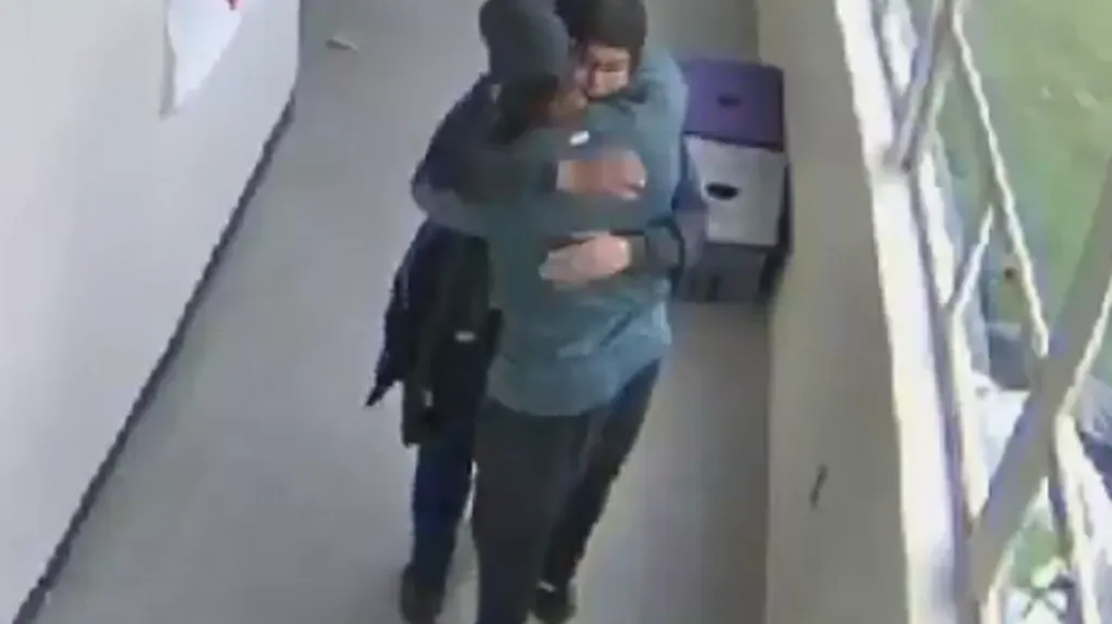 Trenér (zády ke kameře) objímá žáka poté, co ho odzbrojil