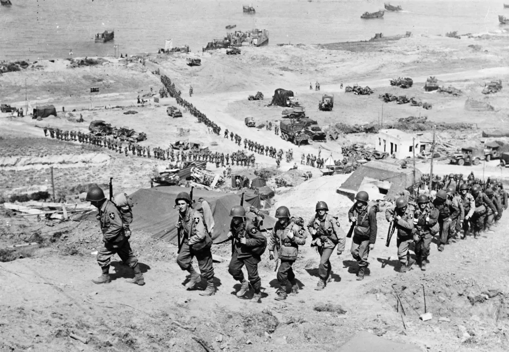Americké posily pochodují do kopce kolem německého bunkru s výhledem na pláž Omaha blízkosti Colleville sur Mer 18. června 1944