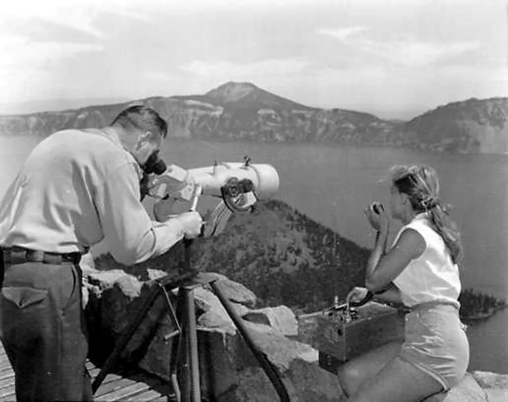 Pracovníci ochrany národního parku informují hasiče o požáru, který zaznamenali pomocí vysoce výkonného dalekohledu na strážní věži v Národním parku Crater Lake v Oregonu. Fotografii vznikla kolem roku 1960