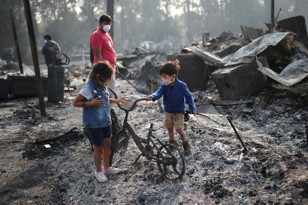 Sourozenci Ashley (3 roky) a Ethan (2 roky) se dívají na spálené kolo v místě, kde stál jejich dům, než požár zničil celou čtvrť domů v Bear Creek v americkém Phoenixu