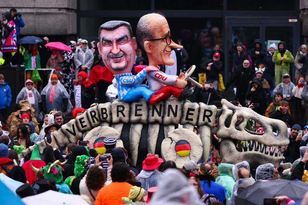 Karnevalový vůz zobrazující německého kancléře Friedricha Merze a bavorského ministerského předsedu Markuse Södera na kostře dinosaura s nápisem Spalovací motor