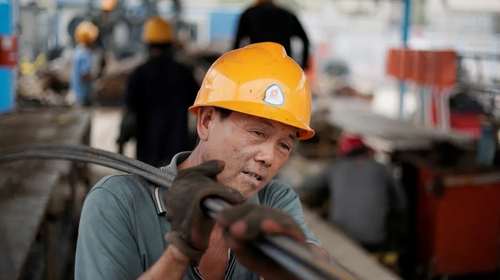 Čínský dělník nese ocelové tyče