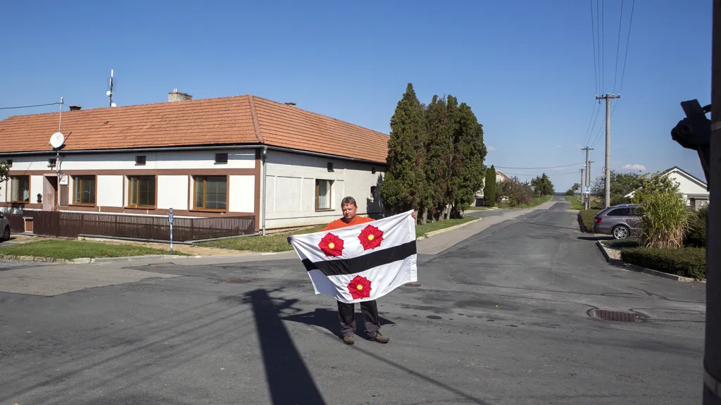Starosta Prokopova na Znojemsku František Kašík s obecní vlajkou na jediné křižovatce ve vsi, která tvoří něco jako náves před obecním úřadem.