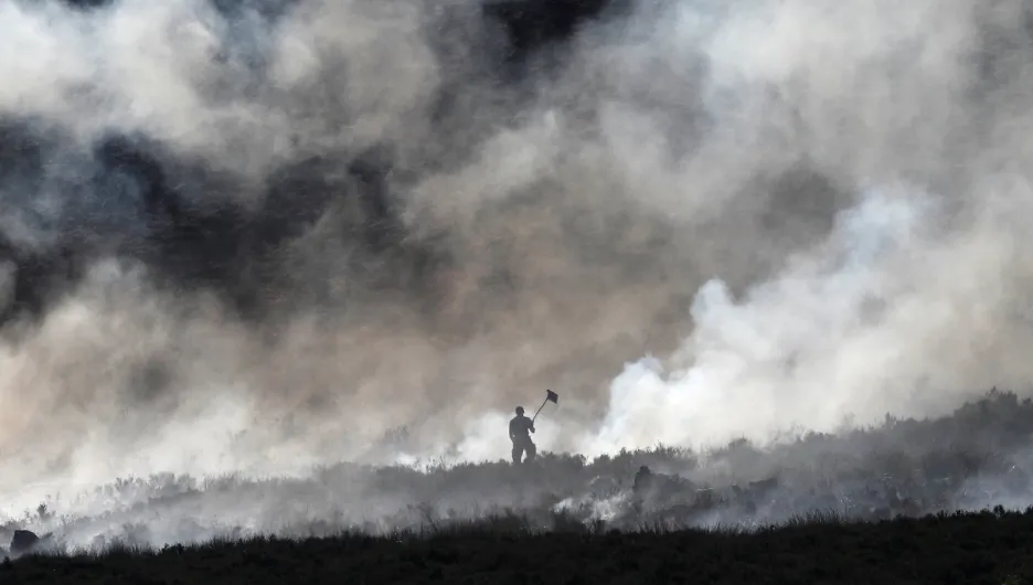 Hasič bojuje s ohněm v doutnajícím vřesovišti nad britským městem Carrwood