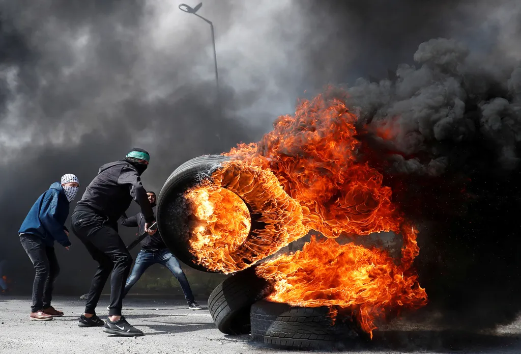 Palestinský demonstrant přesouvá hořící ​​pneumatiku na bariéry během střetů s izraelskými vojsky v blízkosti židovského sídla Beit El na Izraelem okupovaném Západním břehu
