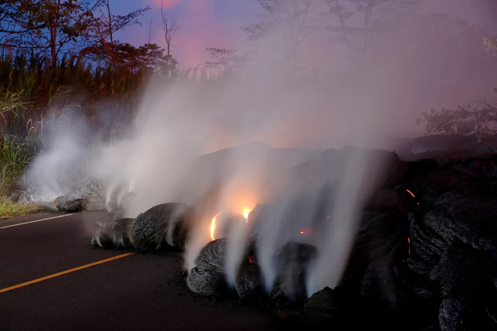Vulkanické plyny stoupají ze žhavé lávy, která se přelévá přes silnici nedaleko města Pahoa na Havaji.