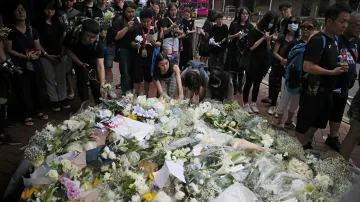 Lidé pokládají květiny k památníku muže, který se v sobotu zabil pádem z budovy, když se snažil instalovat transparent