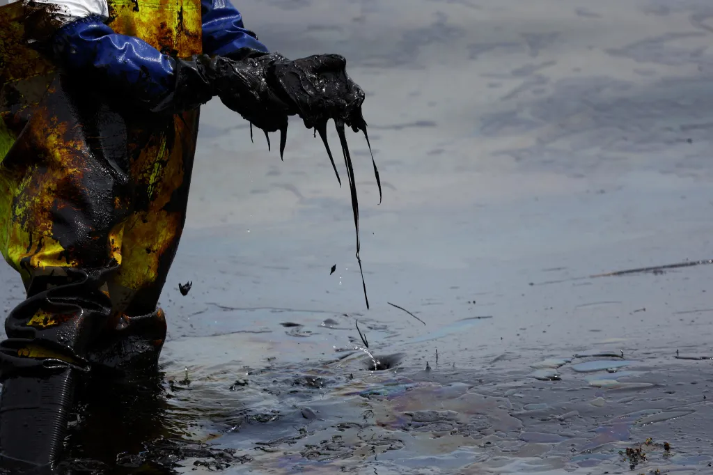 Ropa odkapávající z rukavic pracovníka při odstraňování ropné skvrny