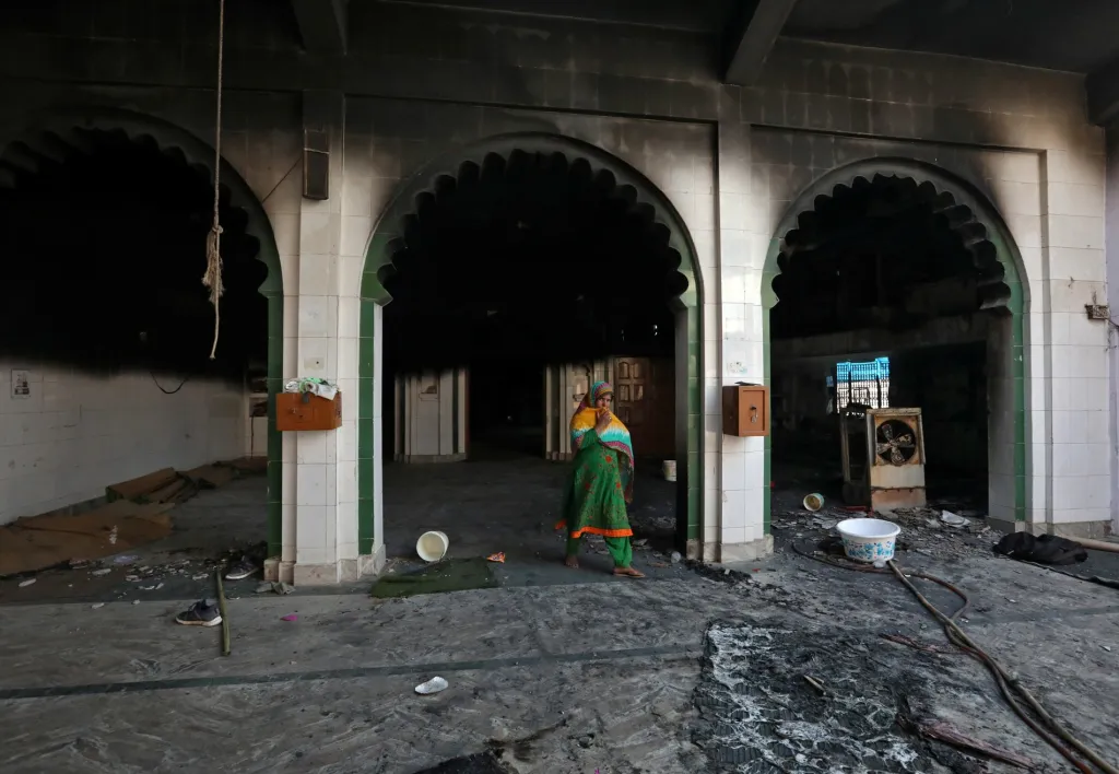 Žena prochází částečně poničenou mešitou, budovu zapálil dav v oblasti nepokojů