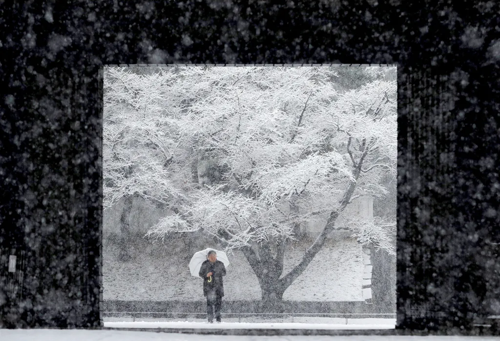 Muž s deštníkem se chrání proti sněhové bouři před japonským císařským palácem v Tokiu