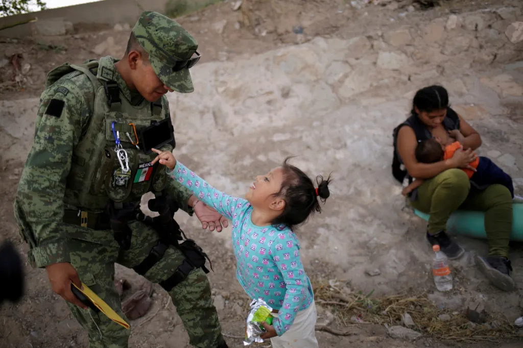 Voják mexické národní gardy si hraje s dívkou, která byla se svojí matkou zadržena během ilegálního přechodu na hranicích s USA, 26.června 2019