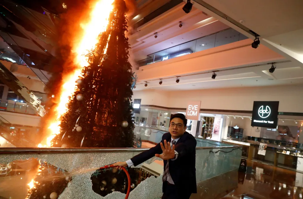 Reakce muže, který se snaží v jednom z hongkongských nákupních center uhasit vánoční strom, jejž zapálili protestující