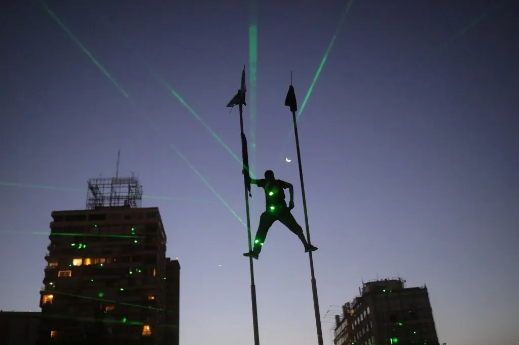 Na demonstranta v Chile svítí zelené lasery, zatímco leze na vlajkové stožáry během protestů v Santiagu, Chile
