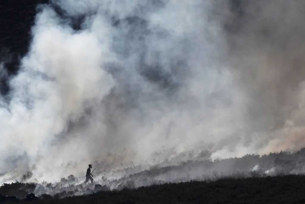 Hasič bojující s ohněm na spáleném vřesovišti nedaleko britského města Carrwood.