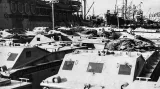 Obojživelná vozidla LVT-1 Amtrac přezdívané Alligator čekají v novozélandském přístavu Wellington 20. července 1942 na nalodění. Tyto vozy uGuadalcanalu zajišťovaly logistickou podporu a přesun tun zásob od pobřeží k frontovým liniím. Jednalo se o jejich první masivní nasazení v boji. Vozidla nebyla pancéřována, což vedlo k těžkým ztrátám v průběhu vyloďovacích operací. V dalším průběhu války bylo vyrobeno mnoho různých verzí, které se staly nezbytnou součástí amerických vyloďovacích operací v P
