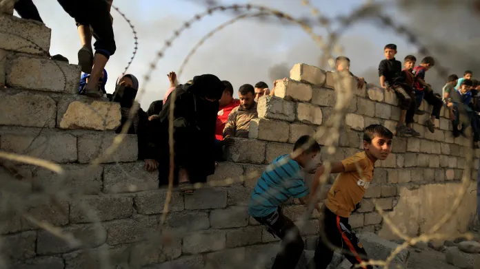 Uprchlíci přelézají zeď, aby se dostali k humanitární pomoci v uprchlickém centru na jih od Mosulu