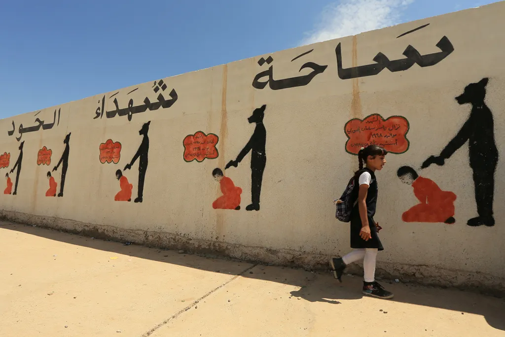 Irácká studentka při cestě do školy kolem jejího plotu pomalovaného propagandou Islámského státu v Mosulu.
