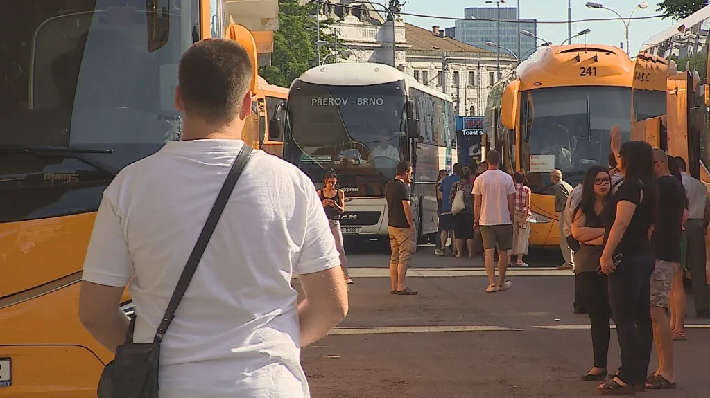 Cestující kličkují mezi autobusy na brněnském nádraží u Grandu