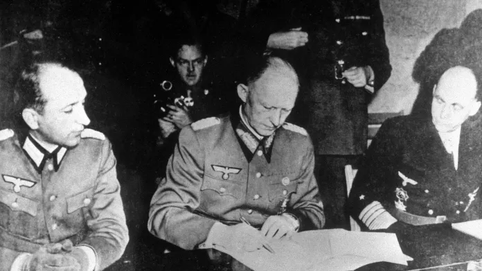 Alfred Jodl – později odsouzený k smrti v Norimberském procesu – podepisuje v Remeši německou kapitulaci. Přihlížejí po jeho levici Hans-Georg von Friedeburg a po pravici Wilhelm Orenius