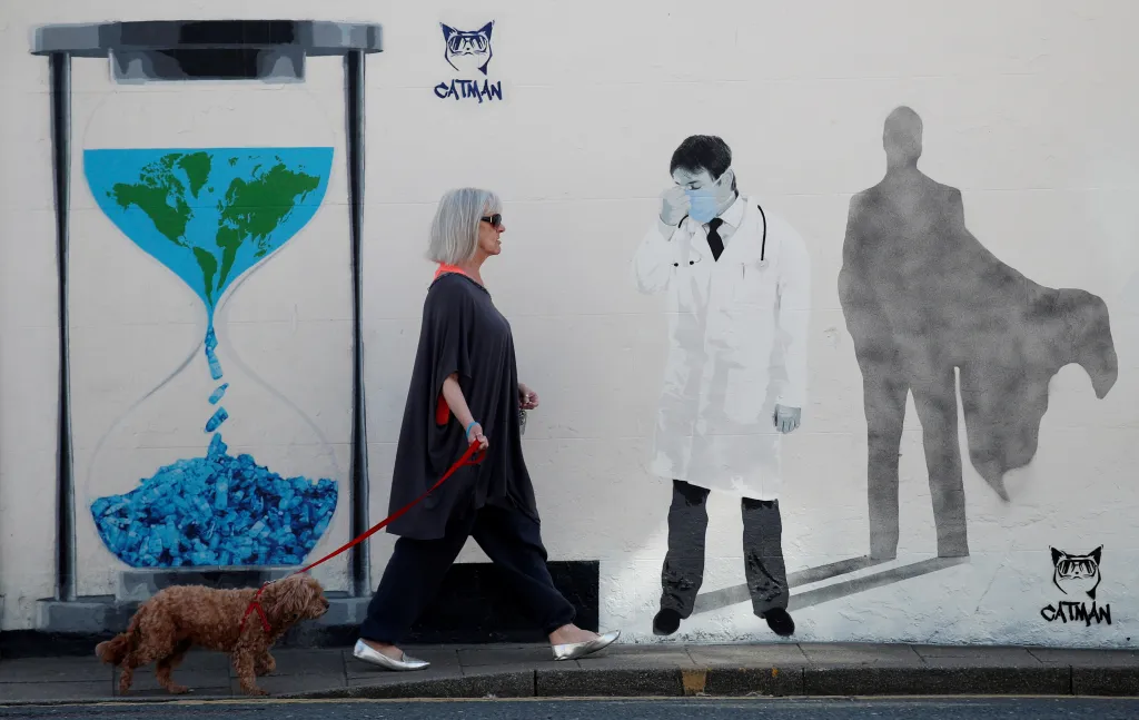Žena se psem míjí novou nástěnnou malbu „Superhuman“ pouličního umělce Catmana vzdávající hold lékařům