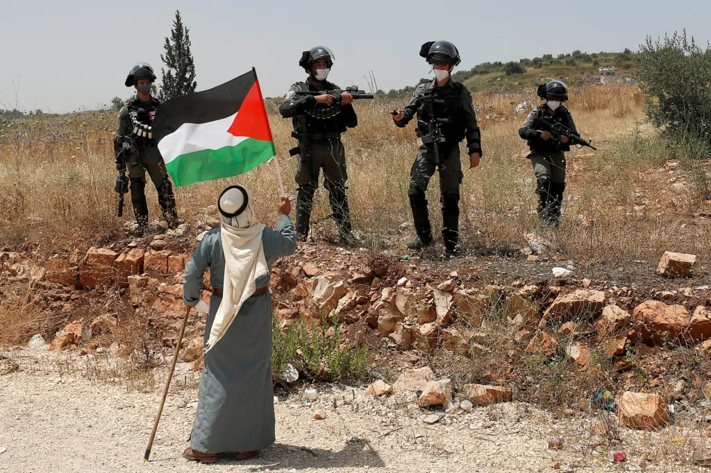 Muž z města Túlkarim drží palestinskou vlajku před izraelskými vojáky během protestu proti izraelskému plánu připojit části okupovaného Západního břehu Jordánu