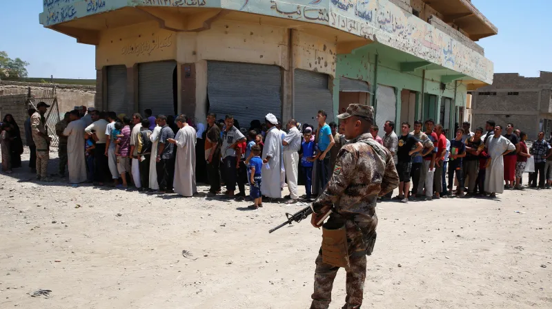 Irácký voják střeží civilisty ve frontě na humanitární pomoc