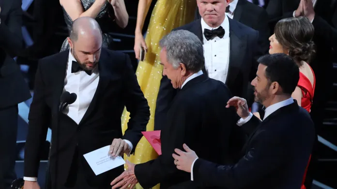 Producent La La Landu Jordan Horowitz drží kartu se správným vítězem Oscarů, vedle něj stojí Warren Beatty a moderátor Jimmy Kimmel. V pozadí dvojice odpovědná za obálky
